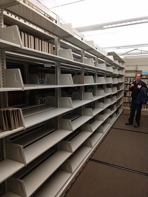 a man stands next to metal library shelves