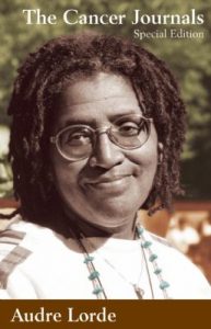 A headshot of Audre Lorde wearing glasses and a necklace