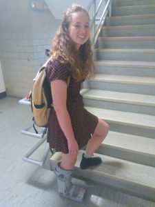 A young woman wearing a medical boot poses on a flight of stairs.