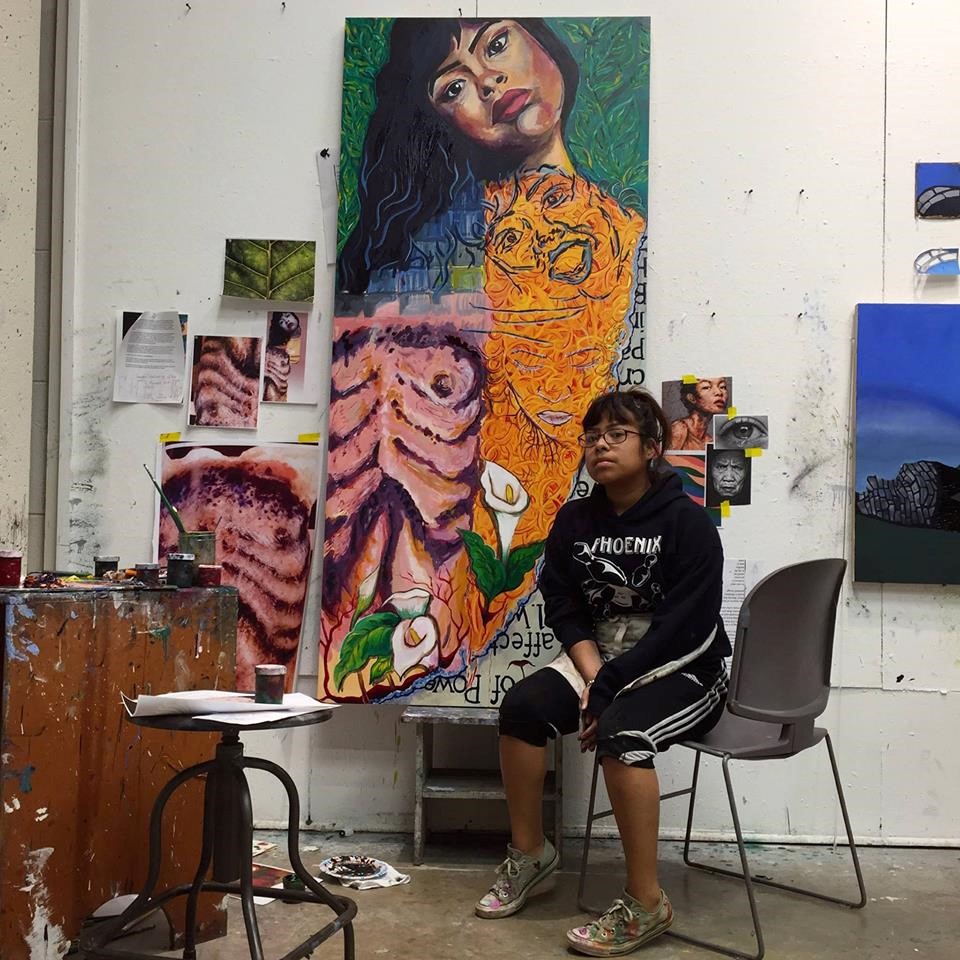 Zarai Zaragoza, a Mexican American Middlebury College senior and studio art major sits in front of colorful art pieces.