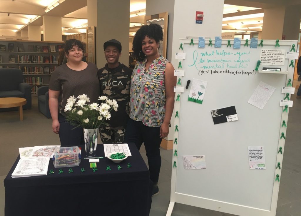 Professor Raquel Albarrán, Myles Maxie and Librarian Katrina Spencer pose with the Mental Health Awareness Month Display.