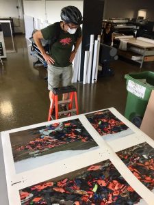 Darren Ell standing on a short ladder inspecting the colors and quality of the triptych prints