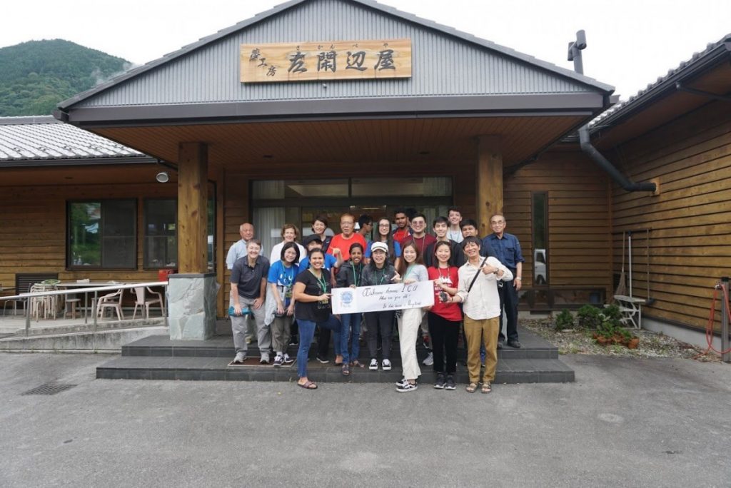 Group photo of Japan Summer Service Learning participants in front of building with sign above in Japanese.