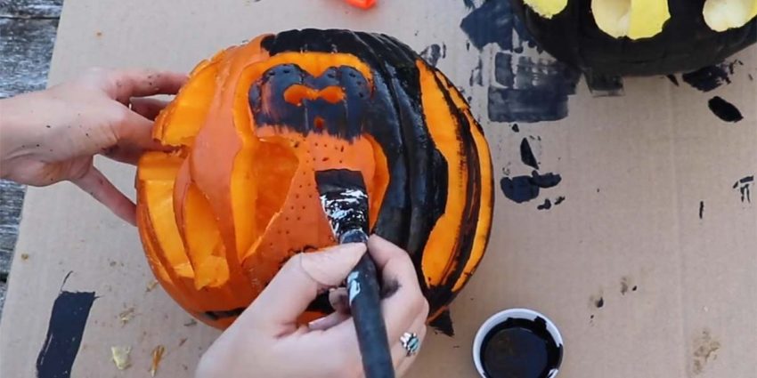 a person carving a pumpkin to resemble an ancient Greek glaux